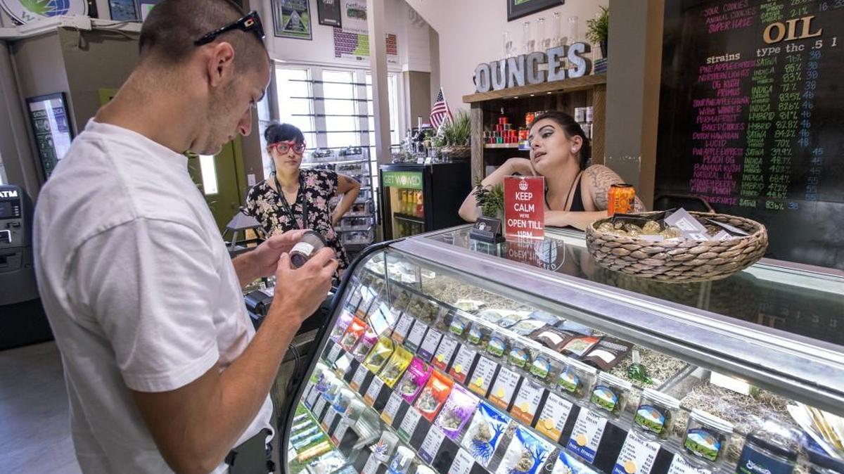 Customer Josh Reed contemplates a marijuana purchase in Tacoma as World of Weed employees Emily Howell, right, and Kayla Beck look on in August. For the first time in state history, residents and visitors spent more on cannabis products than on hard alcohol, based on an analysis of purchase and tax records from two state agencies.