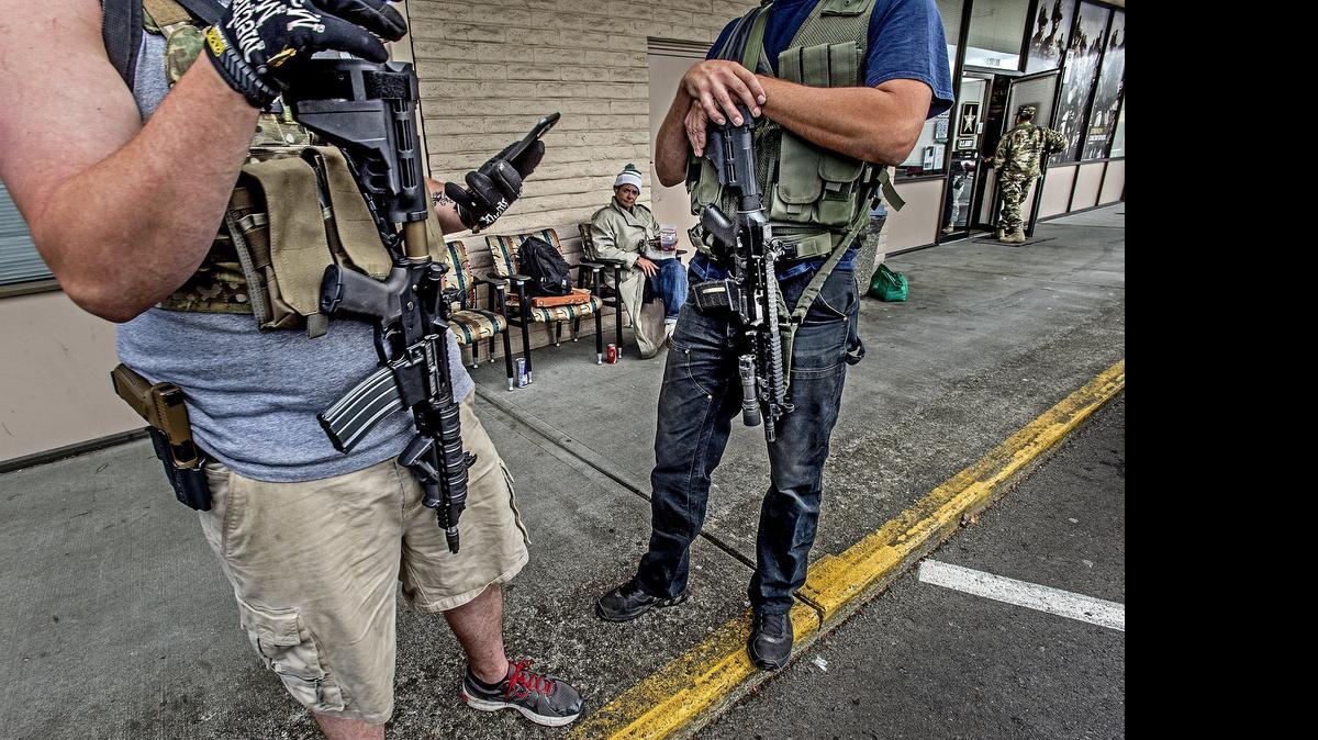 Two men identified only as Zach, 27, left, and his friend Matt, 34, stand outside the U.S. Army Recruiting Office in Spanaway, Wash., carrying AR-15 rifles and holstered semiautomatic handguns. Zach said he called the office earlier in the morning to ask if it would be all right for them to come out. He said they are there because of the shooting at another recruiting office in Chattanooga, Tenn., that left five service members dead. Deanna Rine, seated behind, said “it is all right with me that they are here posing for pictures with their guns.” Rine was just hanging out in front of the recruiting office.

