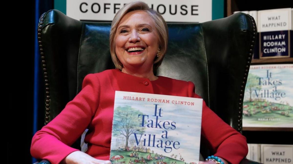 Hillary Clinton, holds her book “It Takes A Village” as she sits on stage at the Warner Theatre in Washington during a September book tour event for her new book “What Happened” hosted by the Politics and Prose Bookstore.