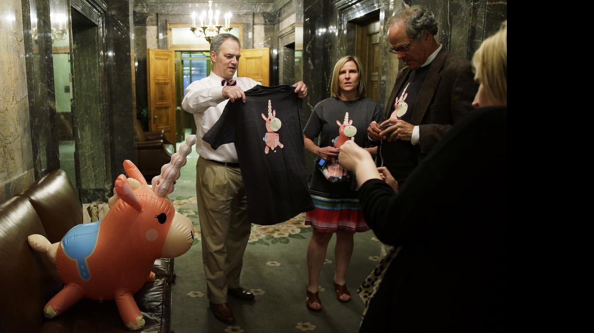 
State Rep. Ross Hunter, left, D-Medina, who chairs the House Appropriations Committee, holds a T-shirt, Tuesday, June 30, 2015, with the image of the Senate Ways and Means committee mascot, the "Balloonicorn" character from the Team Fortress 2 video game, on it as he stands with committee staff members and an inflatable figure of the mascot in the wings of the Senate chamber during a late-night Legislative session at the Capitol in Olympia, Wash.
