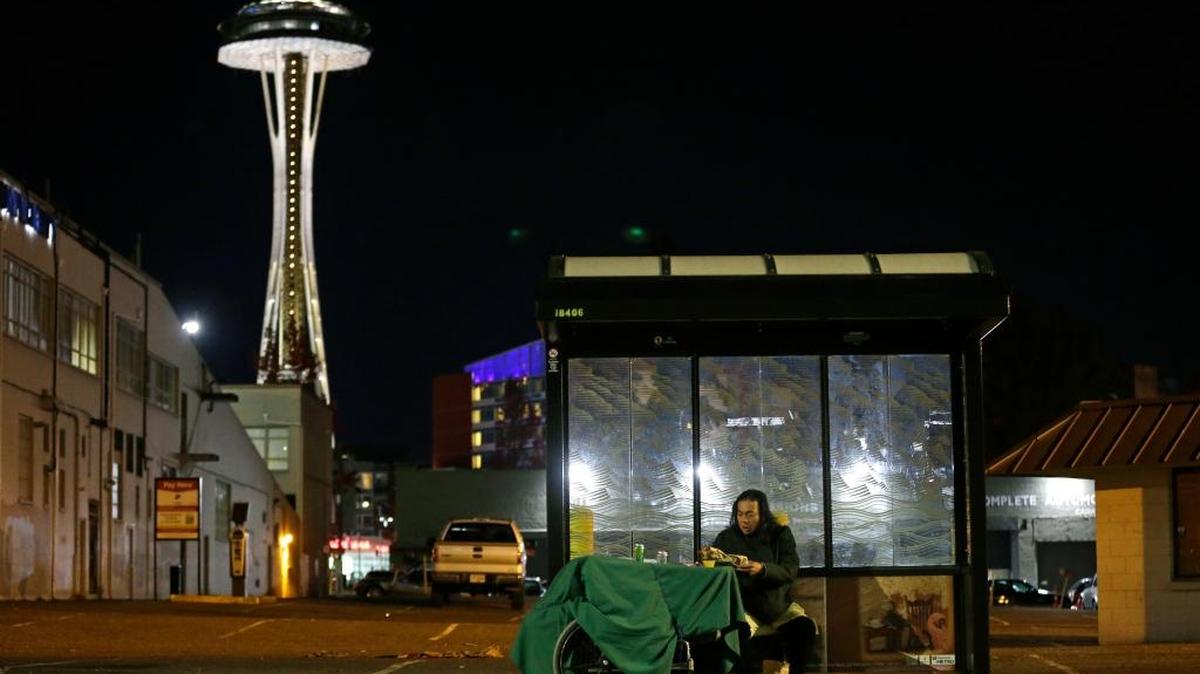 FILE - In this Oct. 30, 2017 file photo, Dave Chung, who says he has been homeless for five years on the streets of California and Washington state, eats a meal before bedding down in a bus shelter in view of the Space Needle in Seattle.
