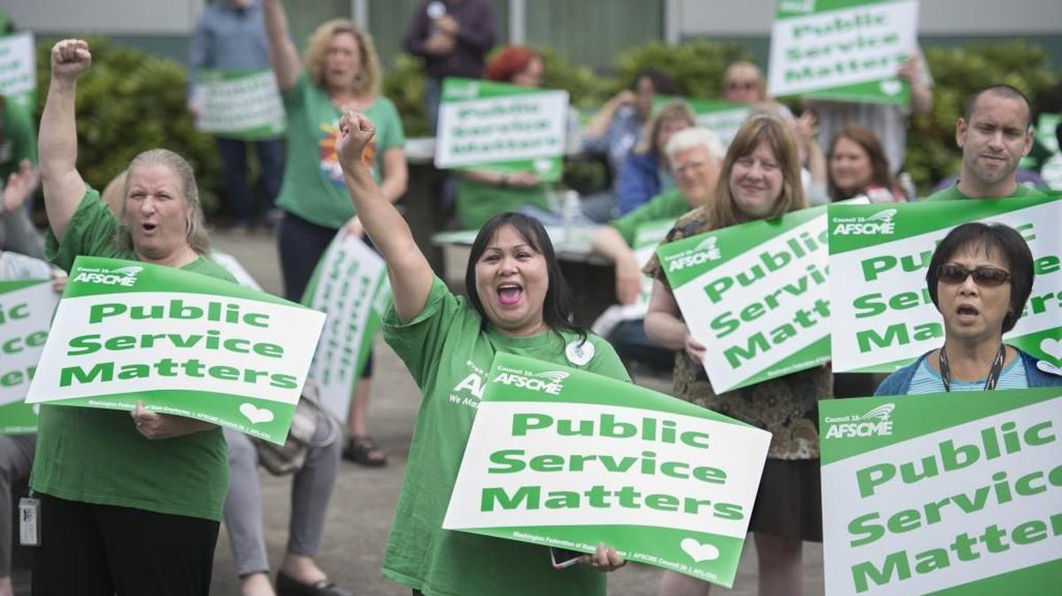 Kellie Klimcazk, left, a coder with Labor & Industries’ International Classification of Diseases unit from Bonney Lake, and Diosy Page, center, an office assistant in L&I’s bill processing department from Lacey, cheer during a rally for the Washington state employees union, AFSCME, at the Labor & Industries Building in Tumwater on Tuesday. Klimcazk has worked for the stte for 15 years, Page for 28 years. State workers say they need higher pay.