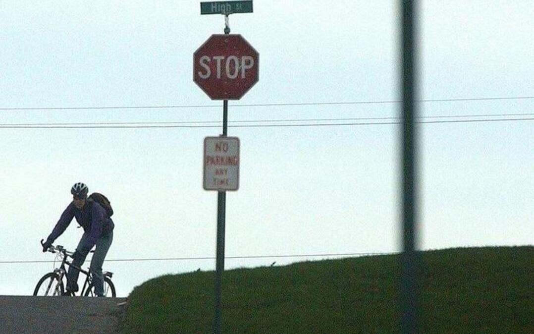 A bicycle rider heads down East Maple Street past a row of stop signs. Bicyclists must stop at the signs just like cars.