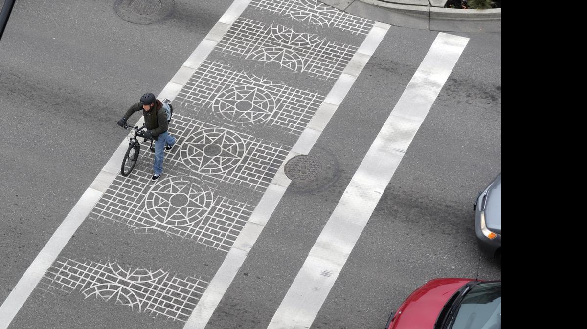 
A bicyclists walks across a decorative crosswalk at the intersection of North State Street and East Holly Street. Downtown Bellingham drivers have a reputation for sometimes running red lights, endangering pedestrians, even those in a marked crosswalk.
