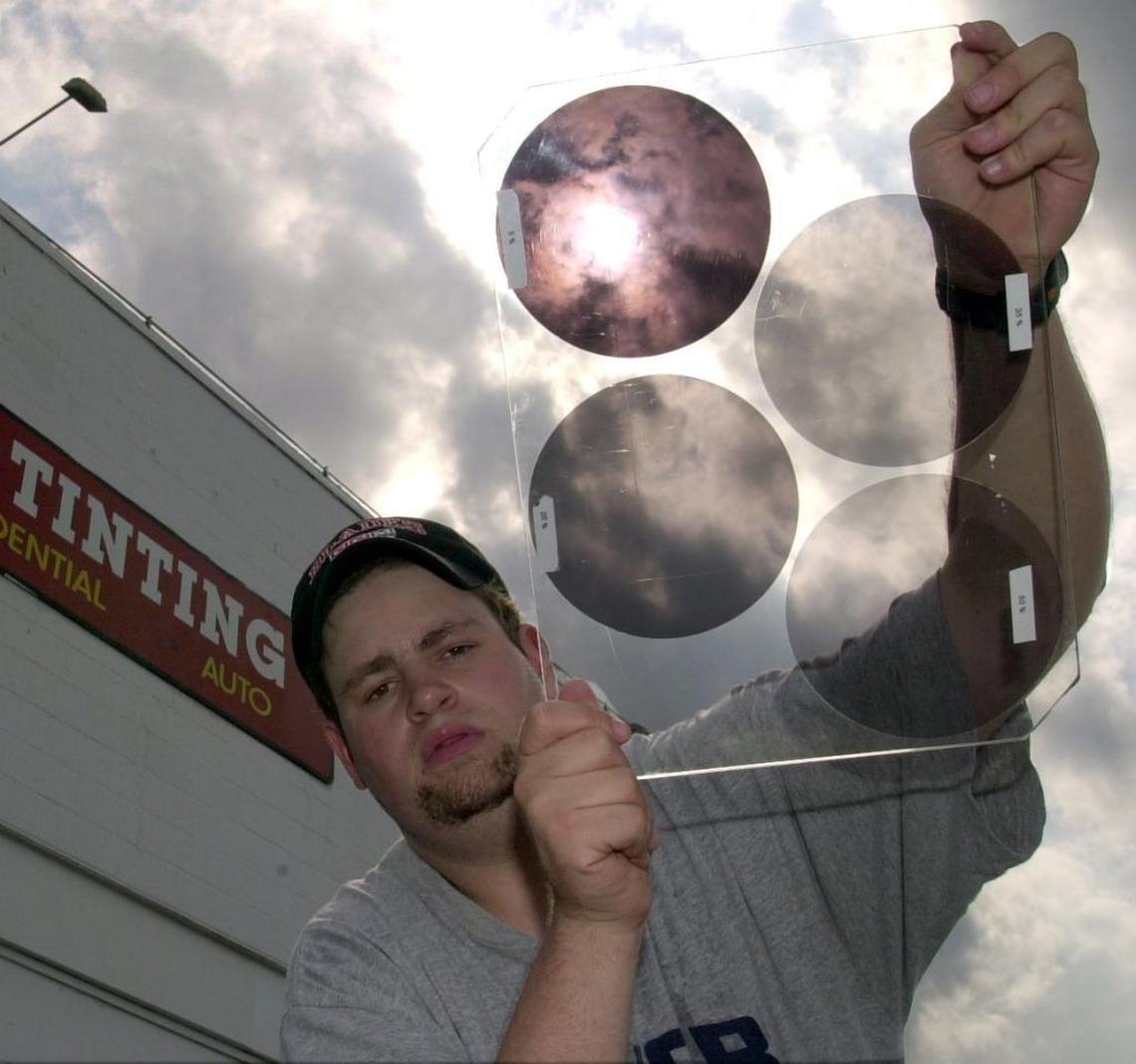 Worker holds a sample of tinted glass applied to cars. The two on the left exceed 24 percent and would be illegal in Washington state. The two on the right, at 5 percent and 20 percent, would be OK.