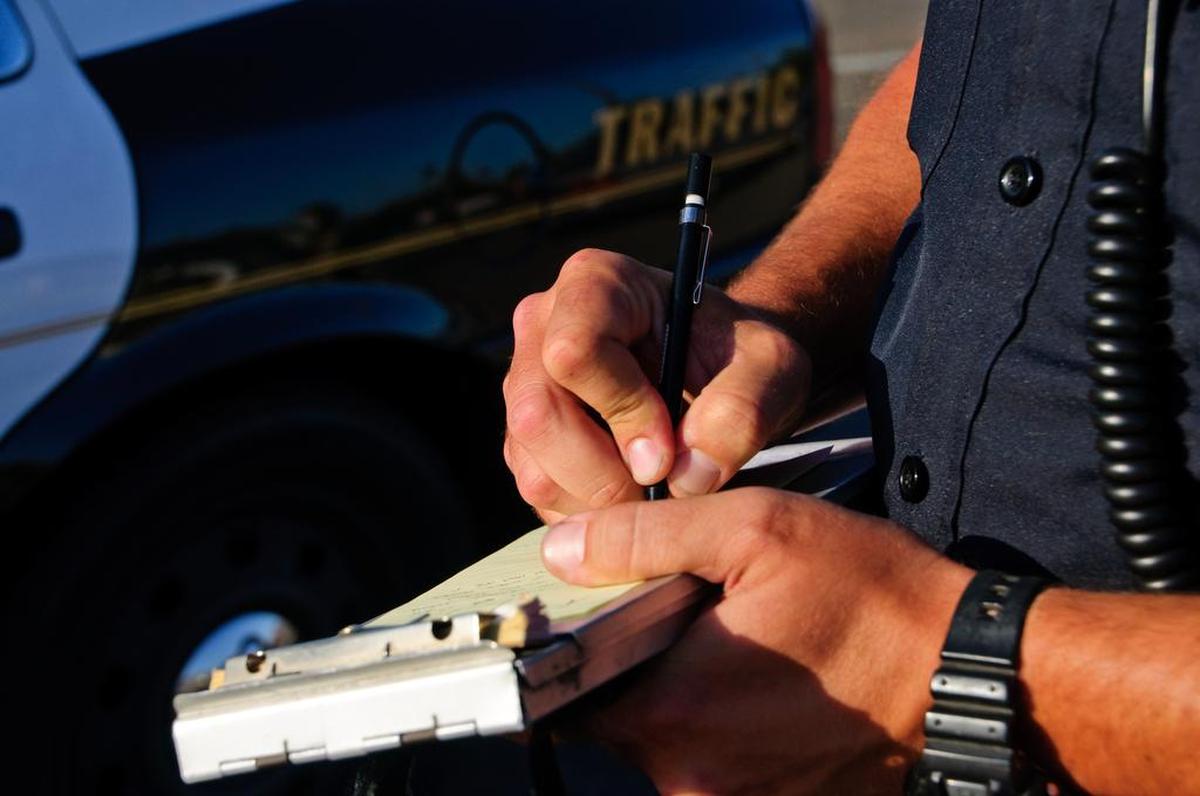 A police officer on the side of the road as he writes a ticket.