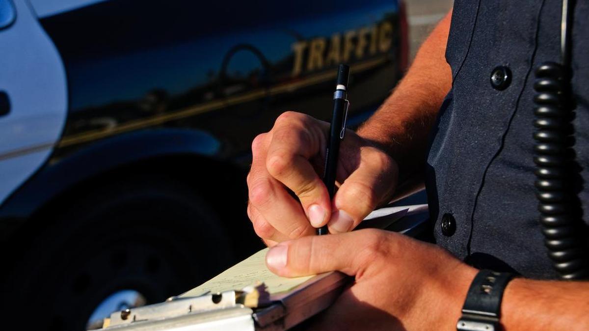 A police officer on the side of the road as he writes a ticket.