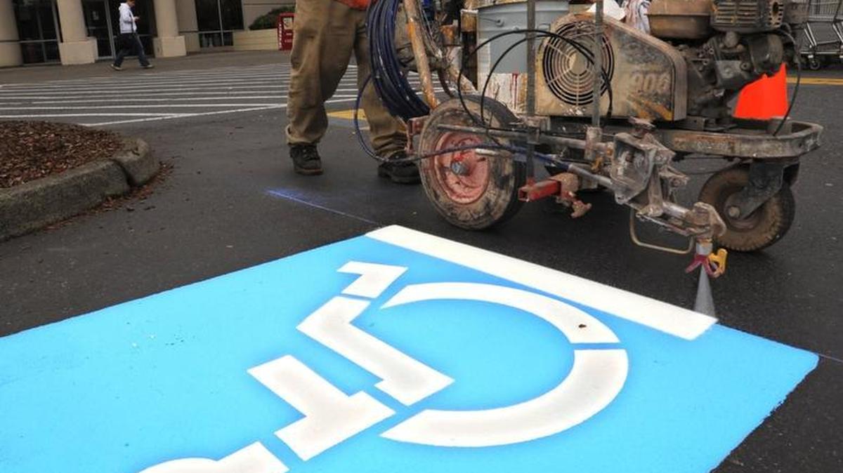 
Pedro Herrjon of Whirlwind Services paints a disabled parking logo in the parking lot outside Macy's Furniture Gallery in 2008. Cars with disabled parking permits or placards from other states or Canada can park in the spaces in Washington state. 
