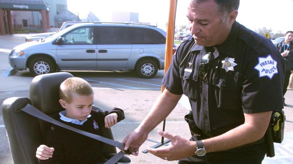 Fresno Police Department Officer John Belli demonstrates the proper way to buckle in a child using a booster seat. In Washington state, all children under the age of 8 or less than 4 feet 9 inches tall must be properly restrained in a child safety seat or booster seat while riding in a car.