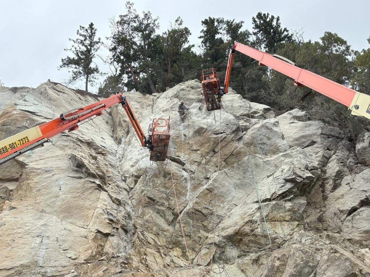 Workers clearing Chuckanut Drive after a rockslide install rock bolts to keep the cliffside together