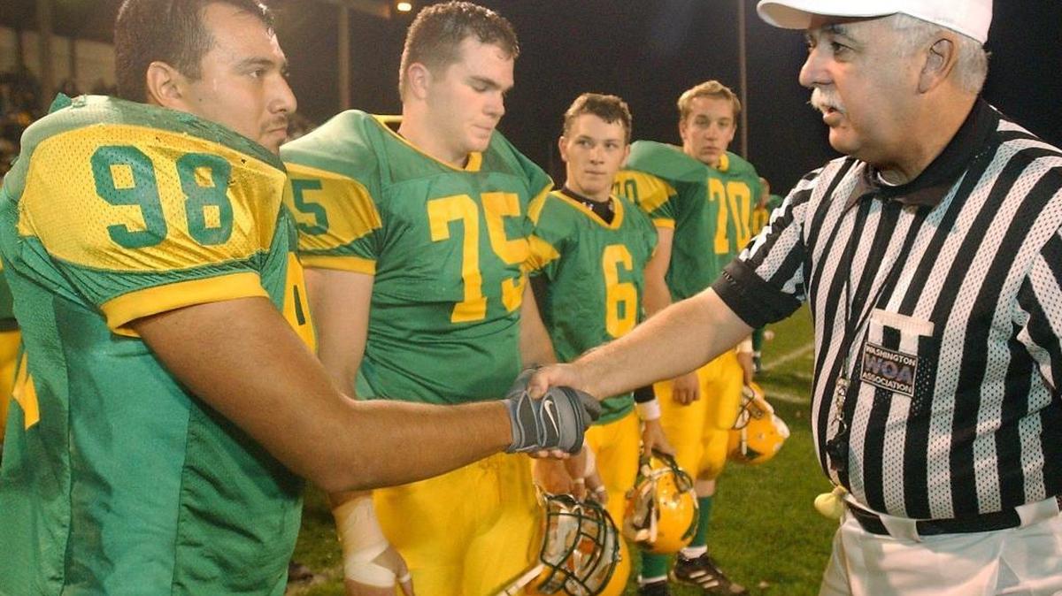Referee Larry LaBree shakes hands with Lynden captain Daniel Salinas as he did with captians Kyle Moore (75), Scott Hardinger (6) and Paul Magrath before escorting them to the middle of the field for the traditional pre-game duties for a 2003 football game. LaBree is retiring from officiating after 45 years of service.