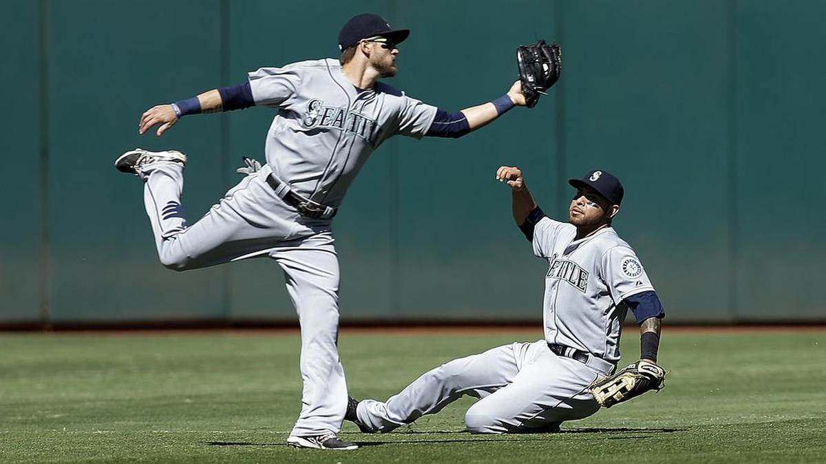 
Seattle’s Shawn O'Malley, left, catches a ball hit by Billy Burns of the Athletics in the seventh inning in front of a sliding Stefen Romero on Sunday in Oakland.
