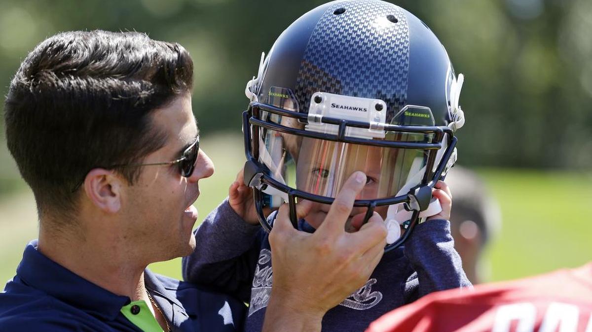 Seahawks assistant coach Dave Canales, left, in 2015 helping his son Benjamin, then 2, try on the helmet of quarterback B.J. Daniels at a minicamp practice. Canales was an assistant for Pete Carroll for 13 years dating to USC.